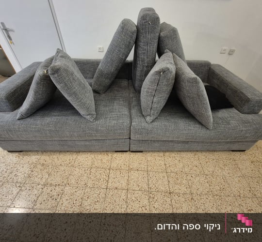 ספה אפורה עם כריות מונחות על רצפה מרוצפת